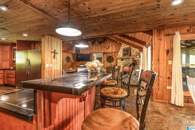 kitchen with pendant lighting, wooden walls, lofted ceiling, and stainless steel refrigerator