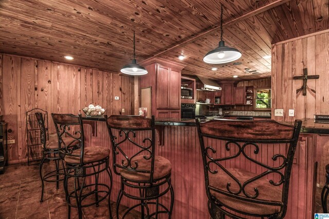 kitchen featuring wall chimney range hood, wood ceiling, oven, hanging light fixtures, and wood walls