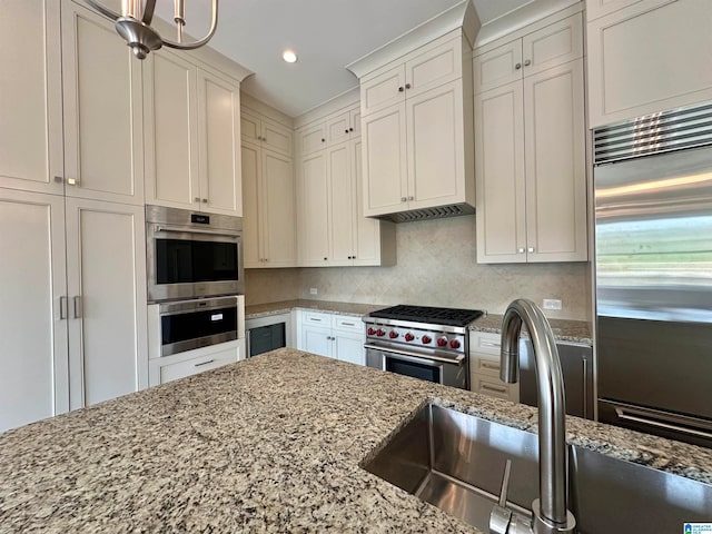 kitchen featuring sink, white cabinets, premium appliances, backsplash, and light stone countertops