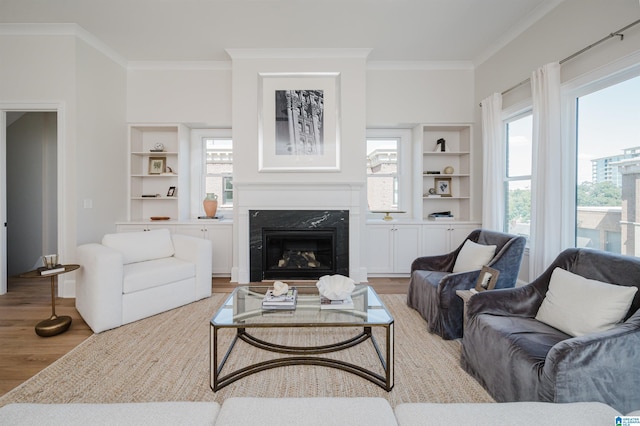 living area with crown molding, light wood-style floors, built in features, and a premium fireplace