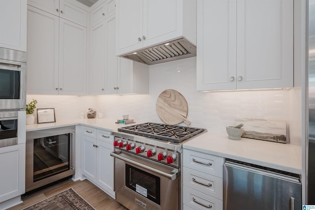 kitchen with light countertops, white cabinets, wood finished floors, wine cooler, and stainless steel appliances