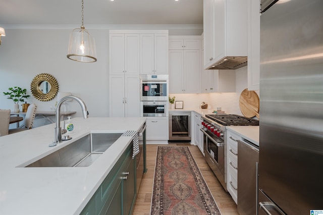 kitchen with light countertops, wine cooler, a sink, appliances with stainless steel finishes, and white cabinets