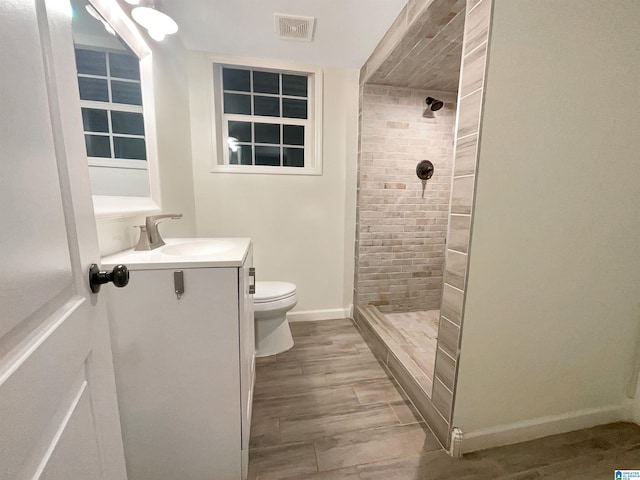 bathroom with toilet, tiled shower, vanity, and hardwood / wood-style floors