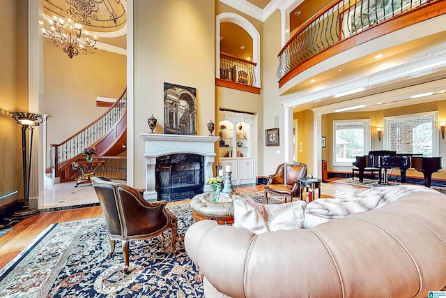 living room with a towering ceiling, a fireplace, hardwood / wood-style floors, a chandelier, and ornamental molding