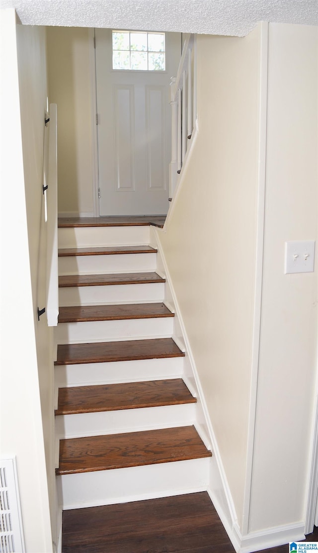 staircase featuring a textured ceiling and wood-type flooring