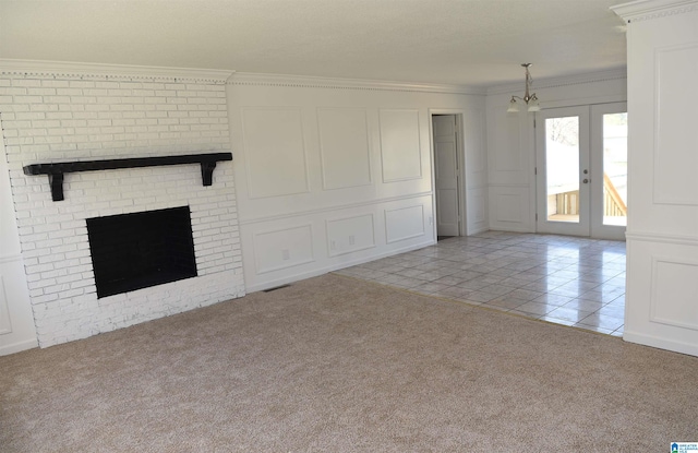 unfurnished living room featuring a notable chandelier, crown molding, french doors, and a fireplace