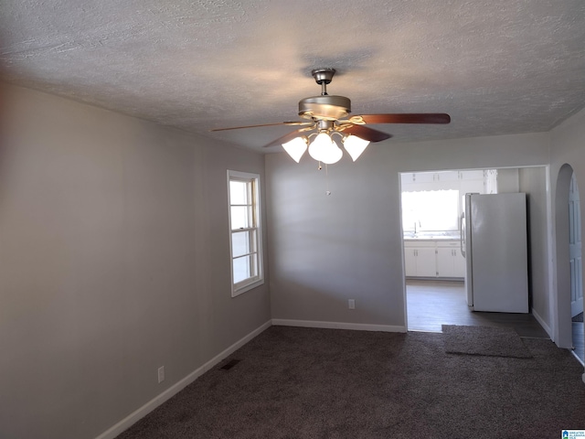 empty room featuring ceiling fan, sink, dark colored carpet, and a textured ceiling