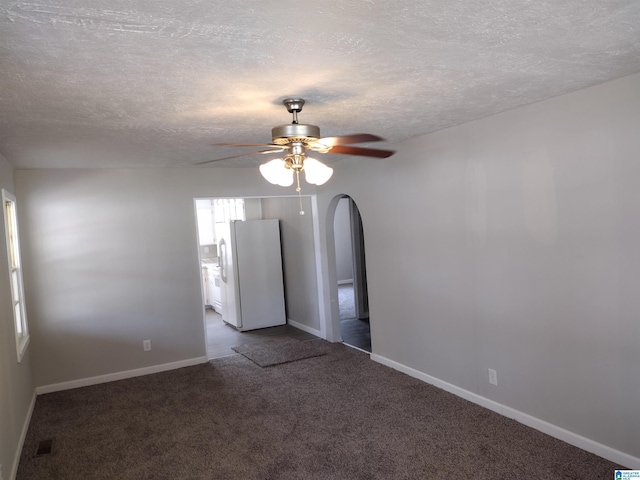 spare room featuring ceiling fan, dark carpet, and a textured ceiling