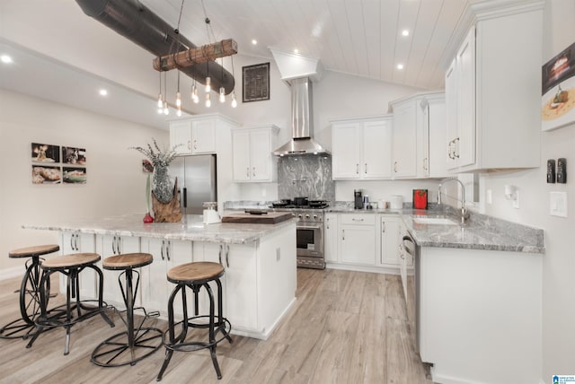 kitchen featuring white cabinetry, light hardwood / wood-style floors, stainless steel appliances, wall chimney range hood, and a kitchen island