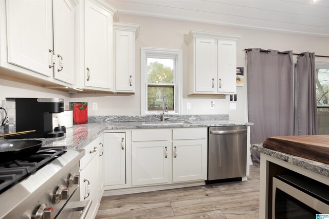 kitchen with white cabinetry, appliances with stainless steel finishes, light hardwood / wood-style floors, sink, and light stone counters