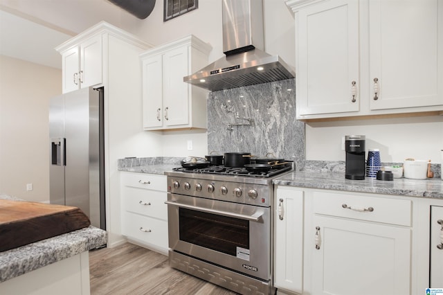 kitchen with white cabinets, wall chimney range hood, light stone counters, and stainless steel appliances