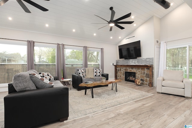 living room featuring a stone fireplace, light hardwood / wood-style floors, ceiling fan, and high vaulted ceiling