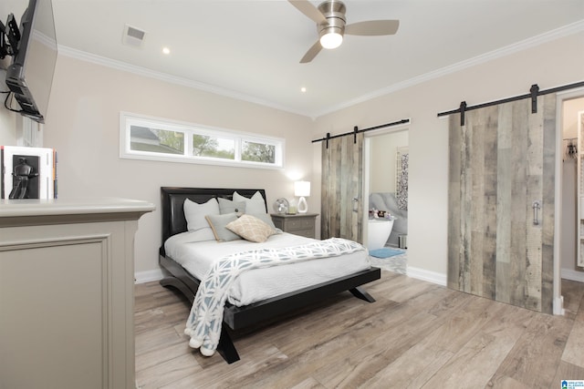 bedroom with a barn door, ensuite bath, ceiling fan, and light wood-type flooring