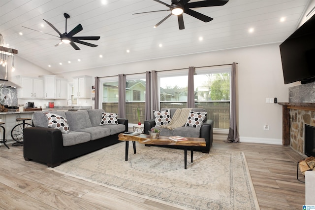 living room featuring a stone fireplace, light hardwood / wood-style floors, ceiling fan, and sink