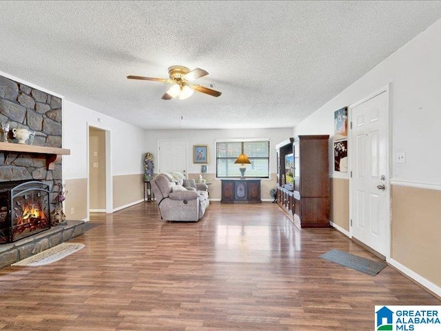 living room with dark wood-type flooring, ceiling fan, a textured ceiling, and a fireplace