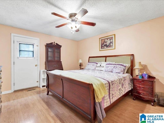 bedroom featuring light hardwood / wood-style floors, ceiling fan, and a textured ceiling