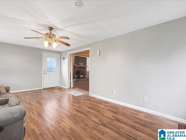 unfurnished living room featuring dark wood-type flooring, a stone fireplace, ceiling fan, and a textured ceiling