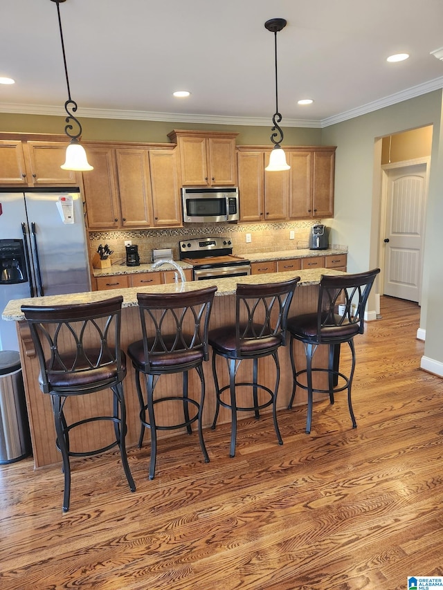 kitchen with light stone countertops, appliances with stainless steel finishes, a breakfast bar, light hardwood / wood-style flooring, and pendant lighting