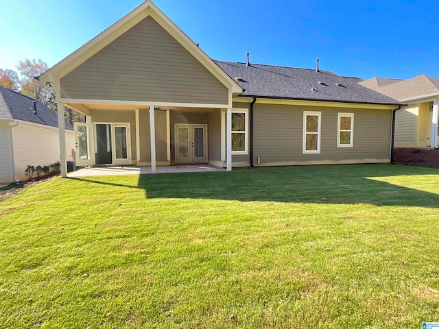 back of house featuring a shingled roof, a lawn, and a patio area