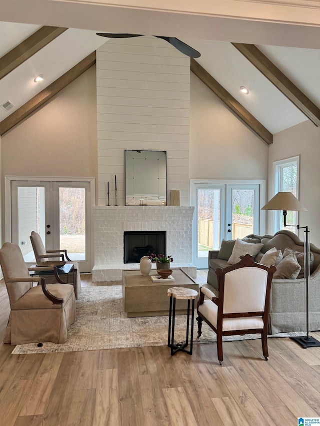 living area with a brick fireplace, high vaulted ceiling, light wood finished floors, and french doors