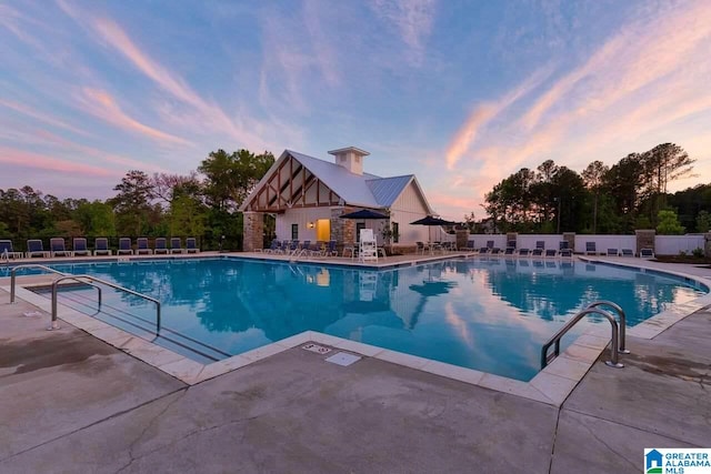 pool at dusk with a patio, fence, and a community pool