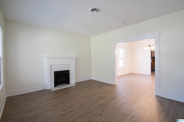 unfurnished living room with a notable chandelier, a brick fireplace, and dark wood-type flooring