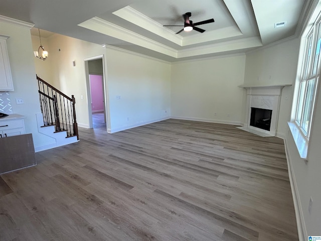 unfurnished living room featuring a high end fireplace, crown molding, stairway, a tray ceiling, and wood finished floors