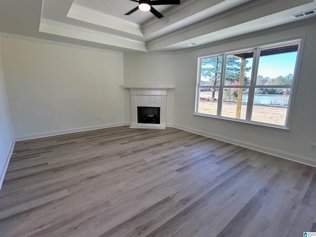 unfurnished living room featuring visible vents, a tray ceiling, ornamental molding, a premium fireplace, and wood finished floors