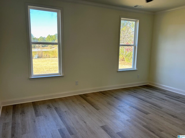 spare room with visible vents, a healthy amount of sunlight, crown molding, and wood finished floors