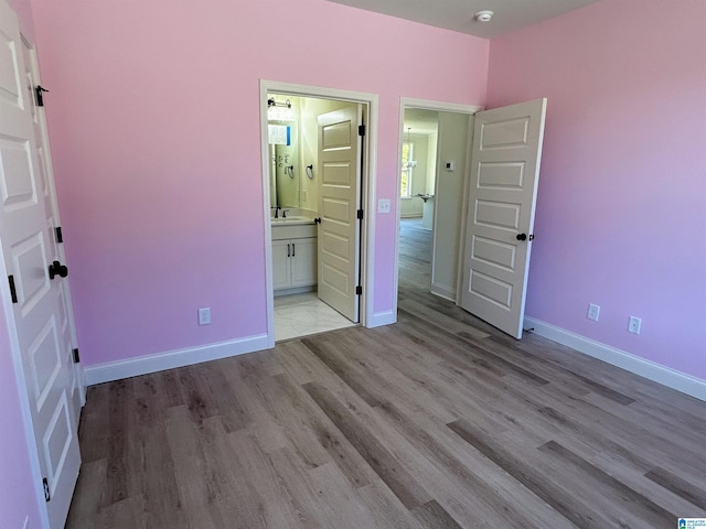 unfurnished bedroom with connected bathroom, wood finished floors, baseboards, and a sink