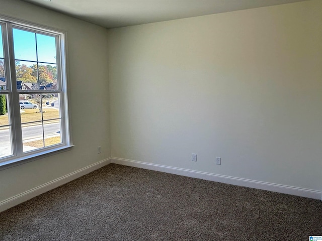 spare room with plenty of natural light, dark carpet, and baseboards