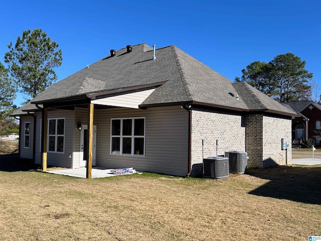 rear view of property with brick siding, a shingled roof, central AC unit, a lawn, and a patio