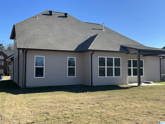 rear view of house featuring a patio, a yard, and roof with shingles