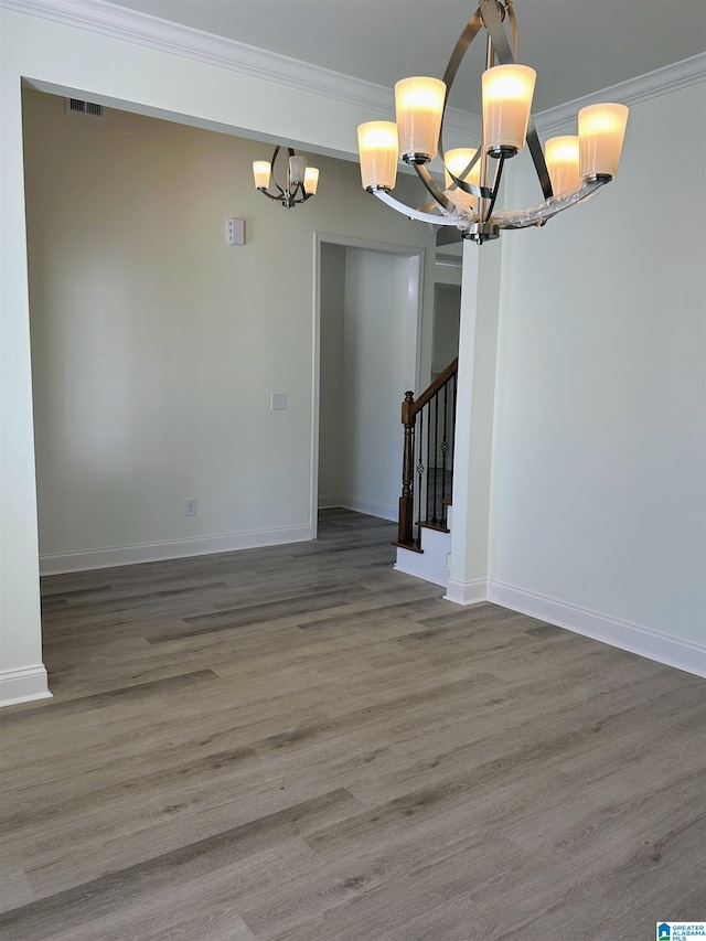 empty room featuring visible vents, stairs, ornamental molding, wood finished floors, and a notable chandelier