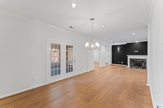 unfurnished living room with light hardwood / wood-style flooring, crown molding, an inviting chandelier, and a tiled fireplace