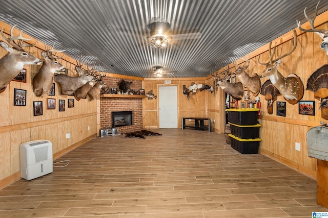 interior space with a fireplace, light hardwood / wood-style flooring, wooden walls, and ceiling fan