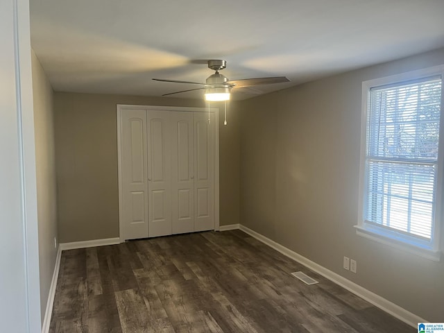 unfurnished bedroom featuring dark wood-type flooring, a closet, visible vents, and baseboards