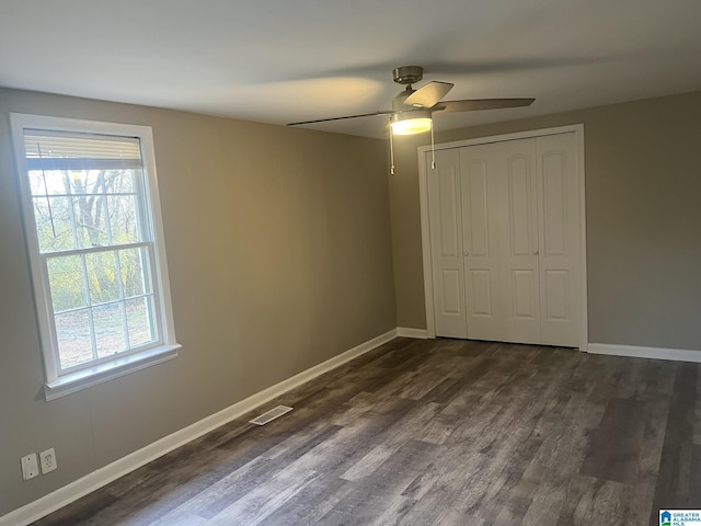 unfurnished bedroom with dark wood-style floors, visible vents, and multiple windows