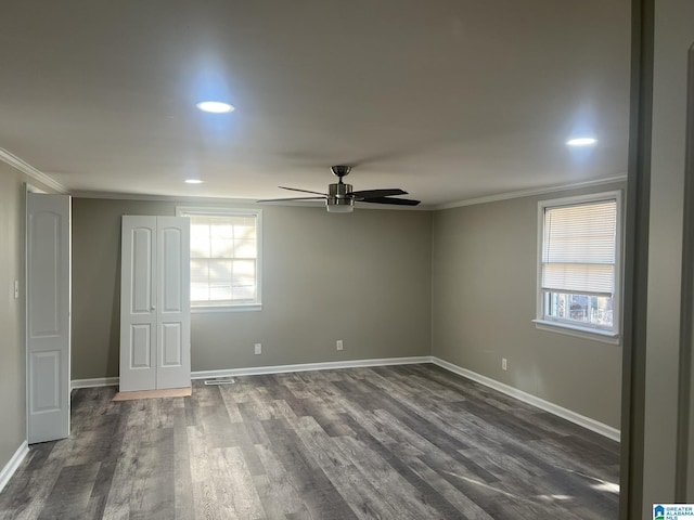 spare room featuring ornamental molding, a wealth of natural light, dark wood-style flooring, and baseboards