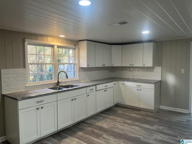 kitchen with dark wood-style floors, a sink, visible vents, white cabinets, and dark stone counters