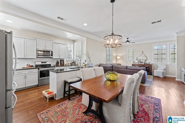 dining room featuring ornamental molding, ceiling fan with notable chandelier, dark hardwood / wood-style floors, and sink