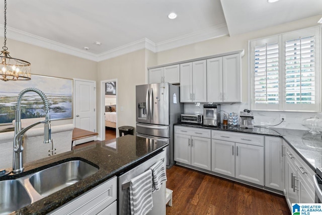 kitchen with appliances with stainless steel finishes, hanging light fixtures, dark wood-type flooring, a notable chandelier, and dark stone countertops