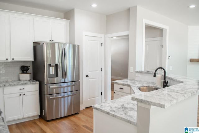 kitchen with tasteful backsplash, stainless steel fridge, sink, white cabinetry, and light hardwood / wood-style flooring