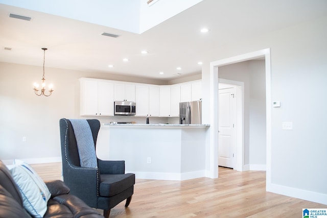 kitchen featuring white cabinetry, an inviting chandelier, appliances with stainless steel finishes, light hardwood / wood-style floors, and pendant lighting