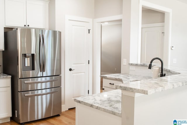 kitchen featuring white cabinets, kitchen peninsula, light hardwood / wood-style flooring, light stone countertops, and stainless steel refrigerator with ice dispenser