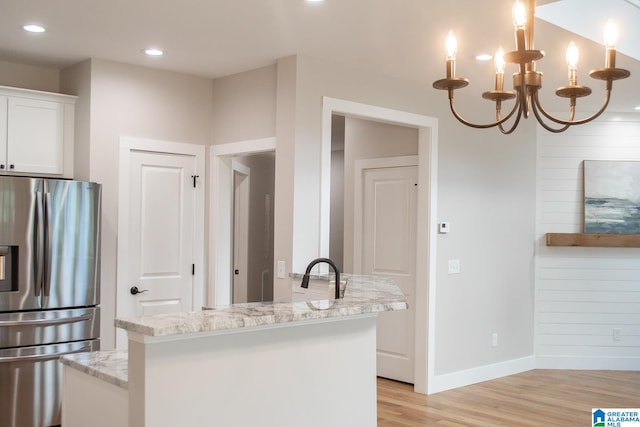 kitchen with stainless steel fridge, white cabinets, light hardwood / wood-style flooring, light stone countertops, and a notable chandelier