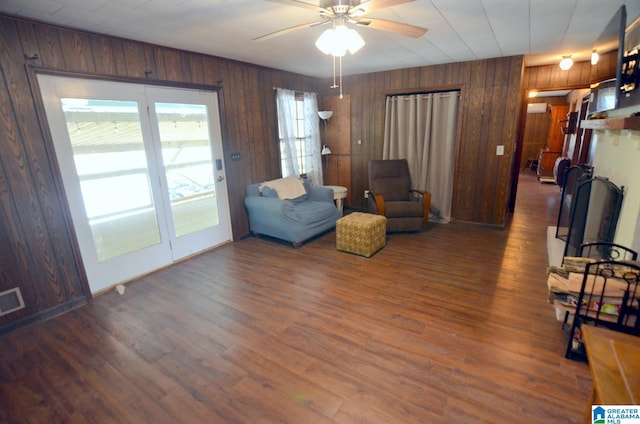 living room with dark hardwood / wood-style flooring, wood walls, and ceiling fan