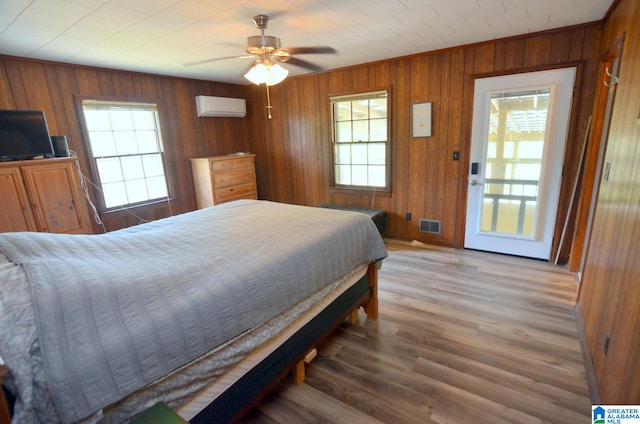 bedroom with hardwood / wood-style flooring, an AC wall unit, wooden walls, and ceiling fan