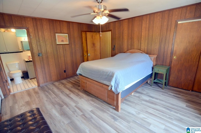 bedroom with ceiling fan, light wood-type flooring, connected bathroom, and wooden walls