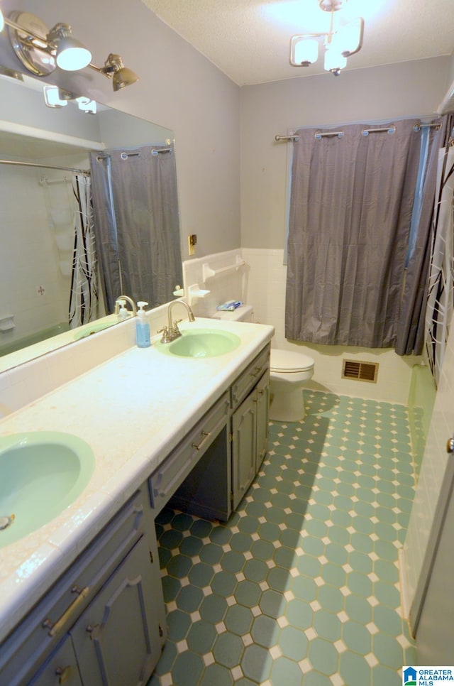 bathroom featuring tile floors, double sink, oversized vanity, toilet, and a textured ceiling